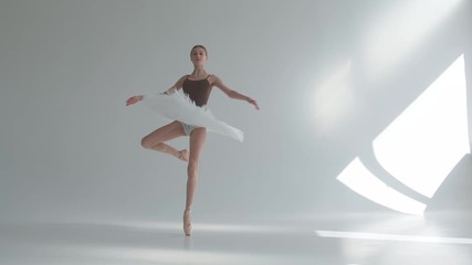 Young ballerina in pointe shoes and white ballet tutu makes pirouette. Shot on a white background in the spacious and brightly lit studio. - Powered by Adobe