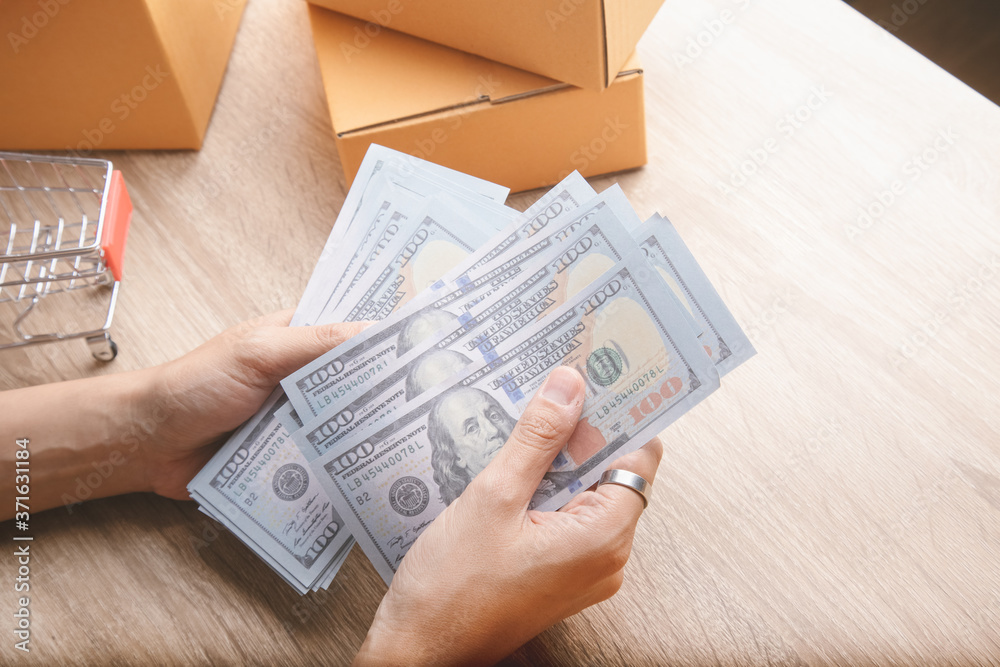 Wall mural top view shot of merchandise table with a lot of earning money (mockup banknote) in hands from e-com