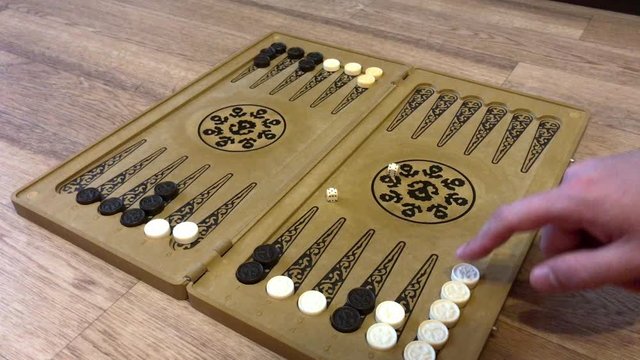Detail of a backgammon game with two dice close up. Male hands rolling two dice and moving checkers on board. Young people playing backgammon while relaxing. 4k.