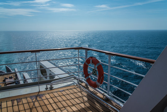 Blick &uuml;ber die Reling (mit Rettungsring) eines Schiffes auf den im Sonnenlicht liegenden Ozean