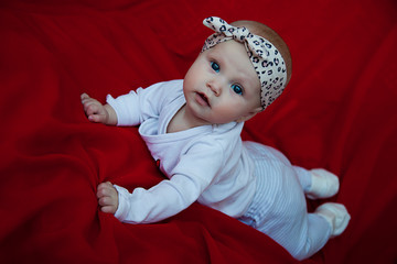 Obraz na płótnie Canvas Cute happy blonde blue-eyed girl 3-4 months old lying on red blanket and looking camera. Conceptual photo for education, healthy childhood, parenting. Perfect caucasian infant. Selective focus
