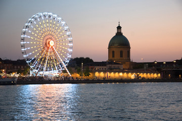 Grande roue illuminée au crépuscule à côté d'une église en ville et sur un fleuve 