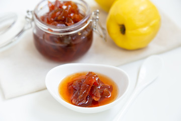 Homemade quince jam in a porcelain bowl with a cup of tea. In the background is a glass jar with jam and quince.