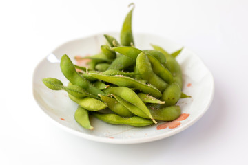 Edamame Nibbles, boiled green soy beans on a plate isolated on white, Japanese food.