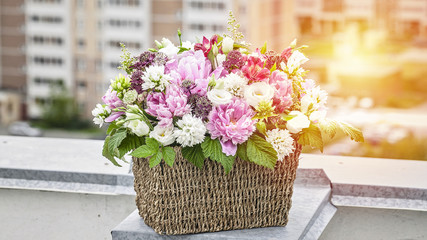 Gift bouquet of flowers in a basket on the background of the roof of the house. Peonies, eustoma, raspberry leaves. WEB banner format