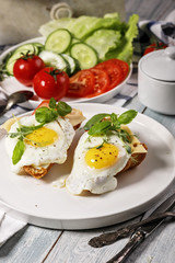 Vertical shot fried eggs with spices, fresh basil and herbs on a white plate. Fresh cucumber and tomato salad. Morning food still life. Tasty breakfast.