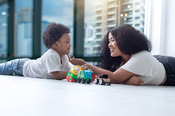 Dark-skinned mother smiling and plays with her son with toy cars on floor at home, happy family