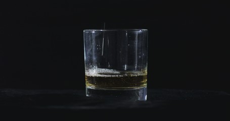 In front of a black background, whiskey is poured into a glass