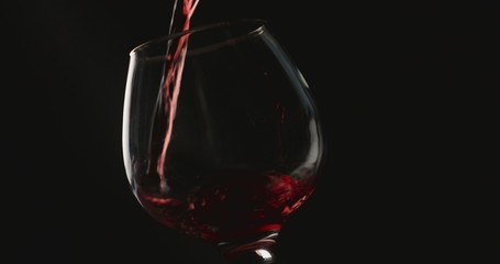 Pouring red wine into a glass, in front of black background