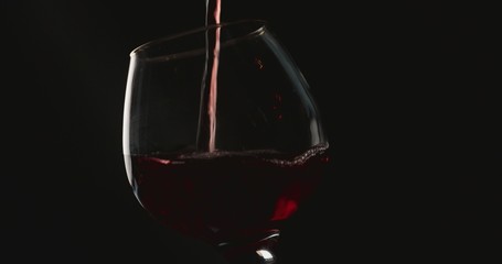 Naklejka na ściany i meble Pouring red wine into a glass, in front of black background