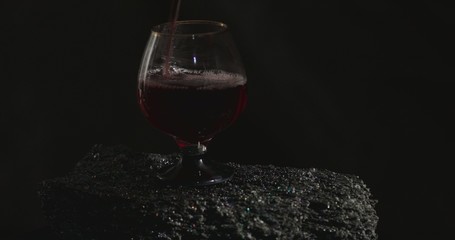 Pouring red wine into a glass, in front of black background