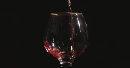 Naklejka na ściany i meble Pouring red wine into a glass, in front of black background