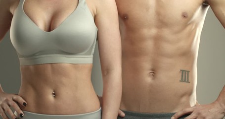 Close-up cropped shot of two bare torsos, sportswoman in sports bra and sportsman turning bodies at camera, showing abs, abdominal muscles after training. Workout, gym and bodybuilding concept