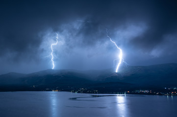 Naklejka na ściany i meble Scenery lightning strike during rainy storm hitting the mountain near lake (toned in cold colors)