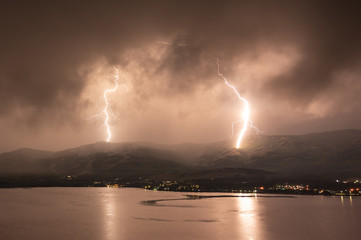 Naklejka na ściany i meble Scenery lightning strike during rainy storm hitting the mountain near lake