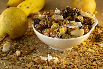 Bowl of granola and cereal with pears and bananas in the background