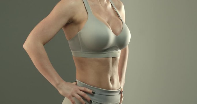 Close-up of sportswoman torso in sports bra, female fitness intructor, showing abs and perfect body, workout in gym. Fit body of young woman with muscles and biceps over studio background