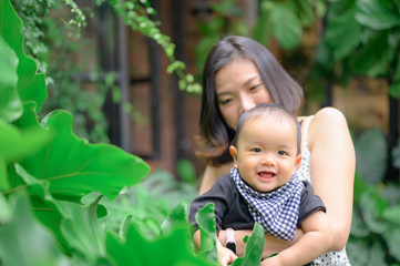 Happy child in the blooming spring garden.Baby boy playing with his mother, enjoying a garden home.