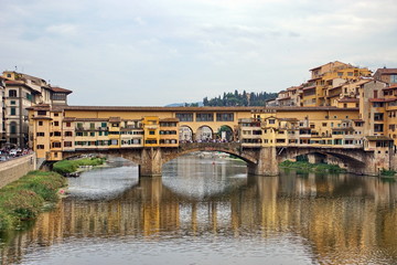 Fototapeta na wymiar The Arno river with the famous Ponte Vecchio (Old Bridge), a medieval stone arch bridge with shops built along it, in Florence, Italy
