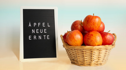 Ripe bright red-orange apples in wicker basket with handles on right and white words in german...