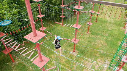 Rope park - climbing center. Hiking in the rope park girl in safety equipment. Roping park. Child boy. Aerial shot. drone.