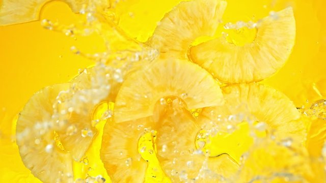 Super Slow Motion Shot of Pineapple Slices Falling into Water on Yellow Background at 1000fps.