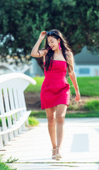 Obraz premium young latin woman standing, long hair brunette in red dress walking, smiling and raising her sunglasses with one hand