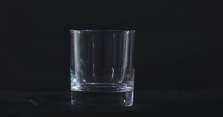 An empty whiskey, alcohol glass against a black background and floating smoke