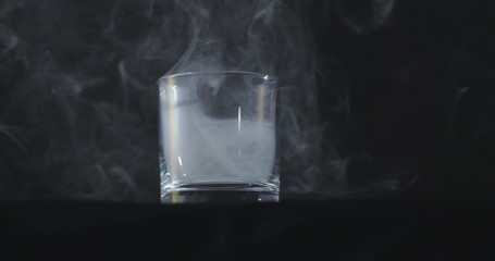 An empty whiskey, alcohol glass against a black background and floating smoke