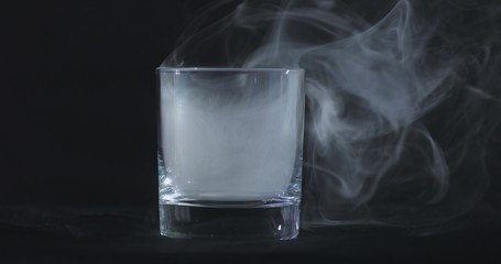 An empty whiskey, alcohol glass against a black background and floating smoke