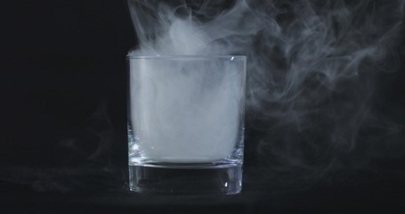 An empty whiskey, alcohol glass against a black background and floating smoke