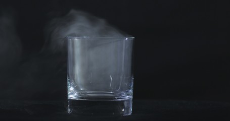 An empty whiskey, alcohol glass against a black background and floating smoke