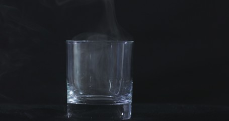 An empty whiskey, alcohol glass against a black background and floating smoke