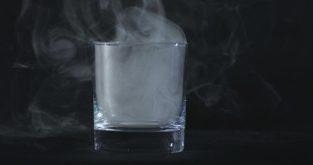 An empty whiskey, alcohol glass against a black background and floating smoke