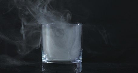 An empty whiskey, alcohol glass against a black background and floating smoke