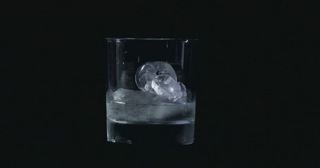 Ice cubes melt in the alcohol, whiskey glass and smoke is floating against a black background
