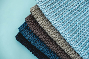 Stack of knitted material from threads of dark blue, light blue, gray colors on a blue background. Top view. Copy, empty space for text