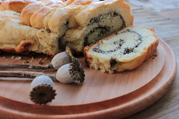 Homemade roll with poppy seeds on round wooden board background. Top view. Selective focus. Slices of cake