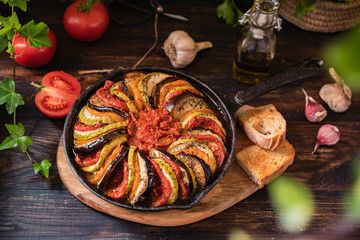 Ratatouille made of zucchini, eggplants, peppers, onions, garlic and tomatoes slices with aromatic herbs, bread. Rustic wooden table. Traditional French food, vegetable, vegan healthy dish. Copy space