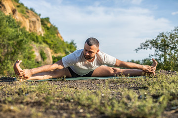 Fototapeta na wymiar Young fitness man doing yoga exercise outdoors at the quarry lake. Handsome young man with a beard doing yoga exercise.