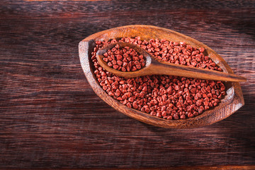 Annatto seeds in bowl on wooden background - Bixa Orellana.