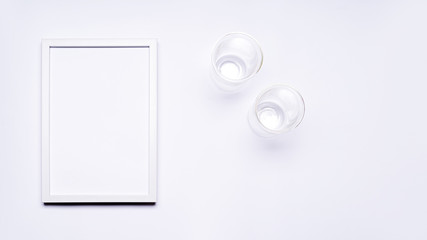 Summer composition. White wooden frame with empty space for text. There are two glasses next to it. Everything is arranged on a white background. Flat top view.