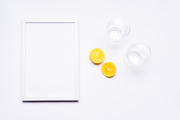 Summer composition. White wooden frame with empty space for text. Next to it, there is a lemon cut in half and there are two glasses. Everything is arranged on a white background. Flat top view.