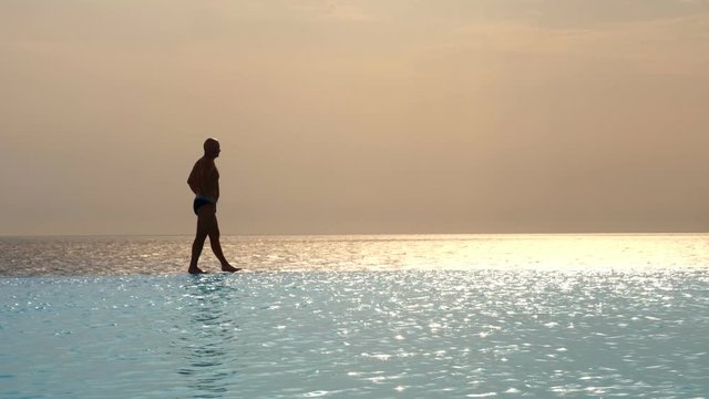dark silhouette, man walking on edge of outdoor infinity pool with panoramic sea view, at sunrise. inspiration, travel and vacation concept
