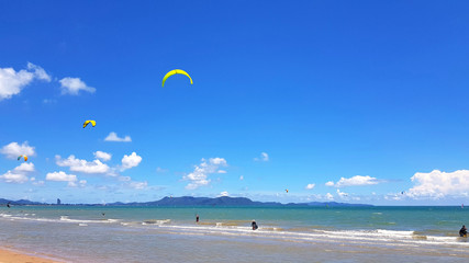 Many people or tourist playing kite surfing on sea with clear blue sky and cloud background and copy space at tropical beach, Chon ฺBuri, Thailand. Extreme activity and sport in summertime 
