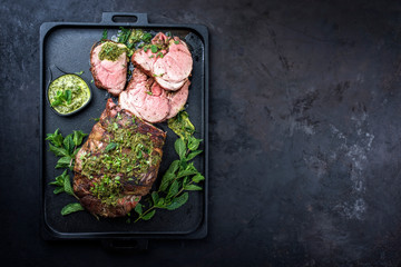 Traditional English barbecue lamb roast sliced with mint leaf and sauce offered as top view in a design cast-iron tray with copy space right