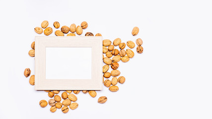 Wooden frame with an empty space for text, lying flat on loosely arranged walnuts. Everything is arranged on a bright table. Flat, top view, no people.