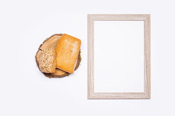 Still life of organic products. Empty wooden frame with space for text. Organic bread stacked on a round piece of wood. Everything is placed on a bright table. Flat, top view, no people.