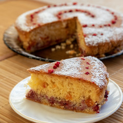In the foreground- a triangular piece of biscuit, soaked with a layer of currant jam and pieces of dried apricots. The whole cake is in the background. The top of the cake is decorated with cherries.