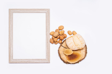 Still life of organic products. Empty wooden picture frame. Walnuts, organic bread and natural honeycombs arranged on a round piece of wood. Everything is placed on a bright table. Flat, top view.